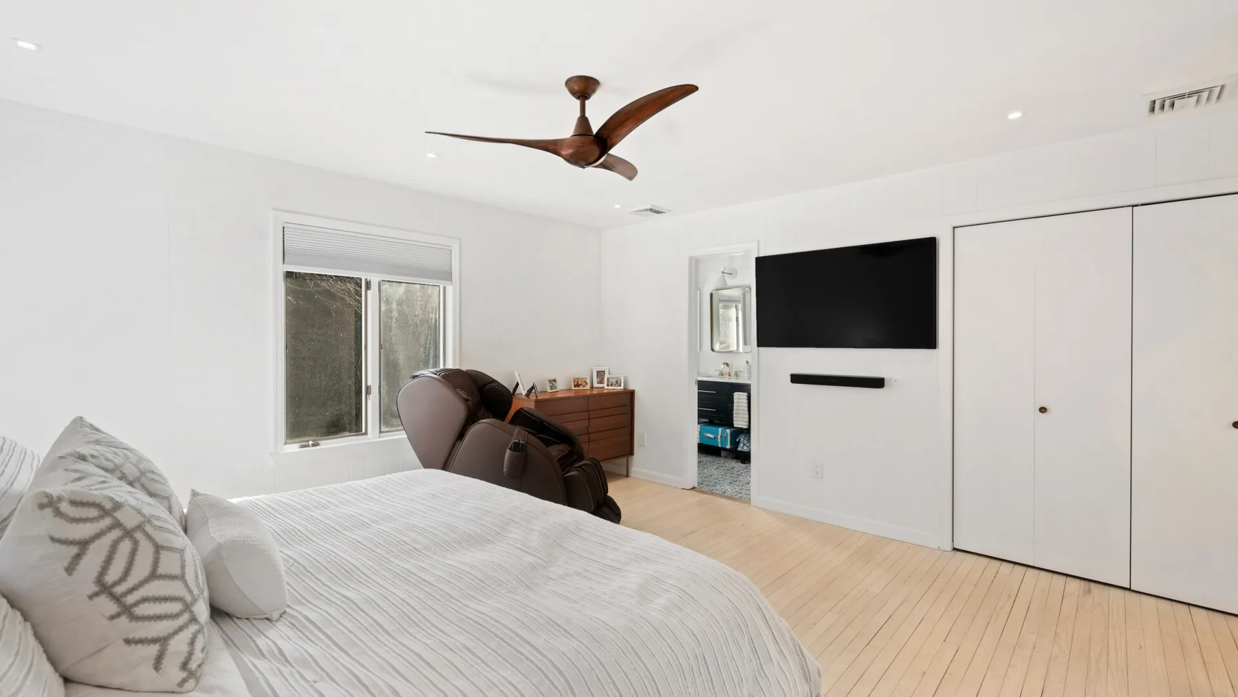 Un dormitorio luminoso con una cama, un televisor en la pared y un ventilador de techo.