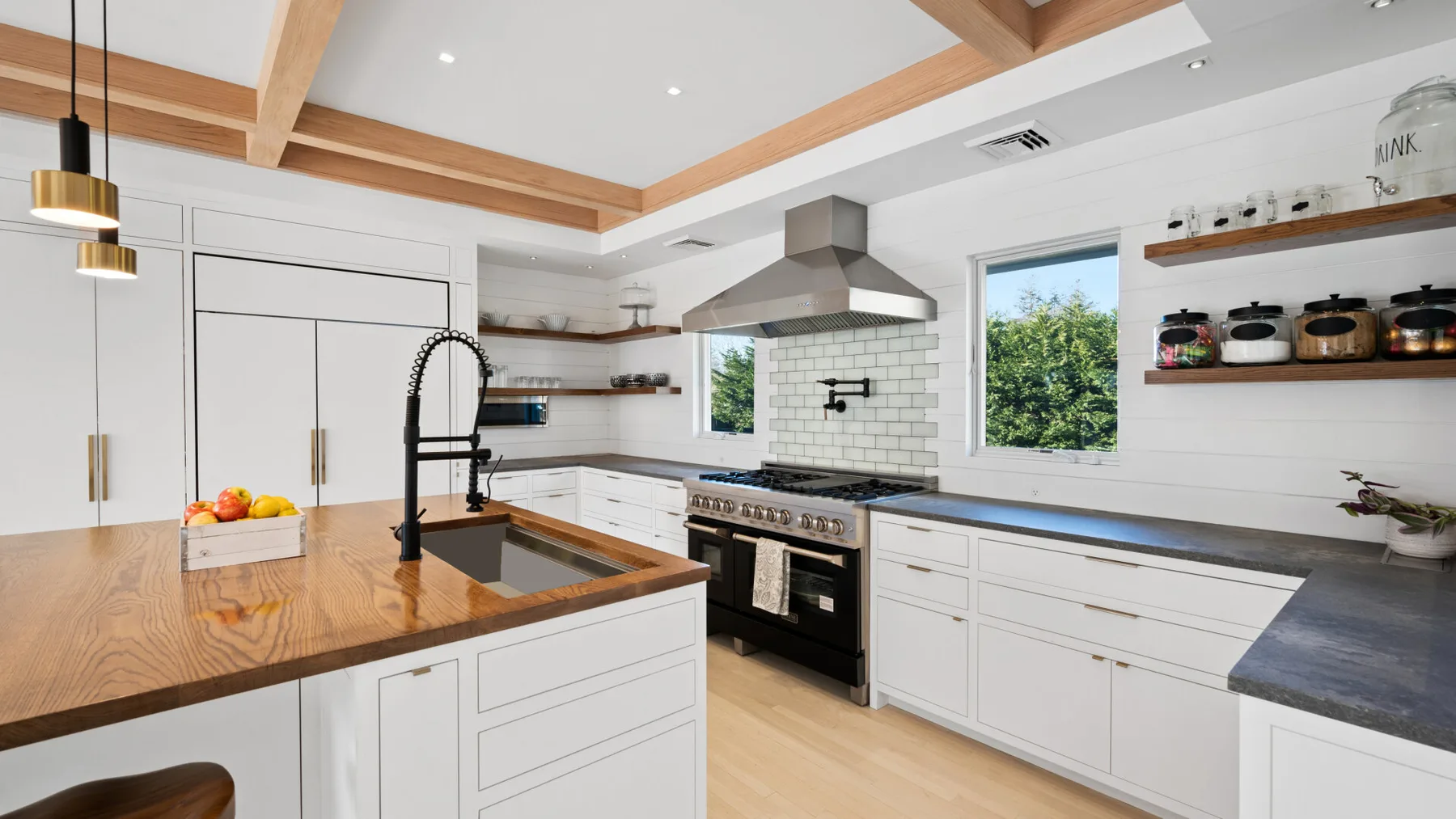 Una cocina luminosa con gabinetes blancos, una isla de madera y una estufa de acero inoxidable.