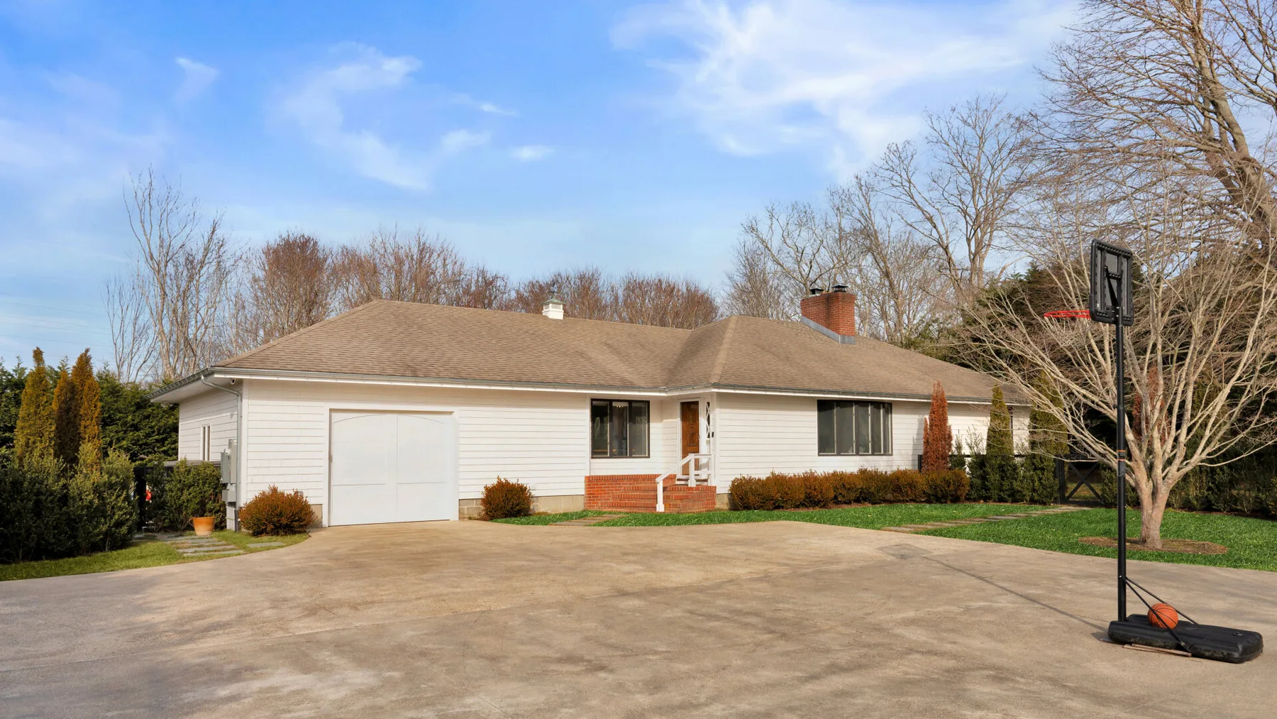 Una casa de una planta da a una amplia entrada pavimentada y una canasta de baloncesto.