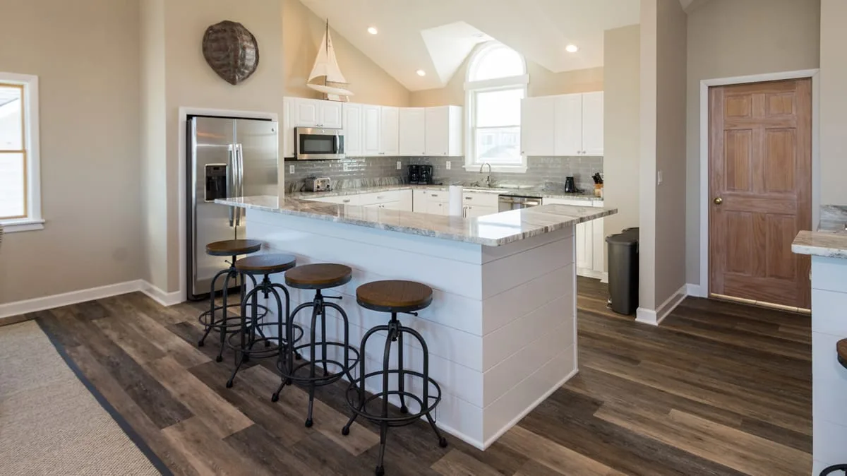 Una cocina luminosa cuenta con una isla grande con asientos y gabinetes blancos.