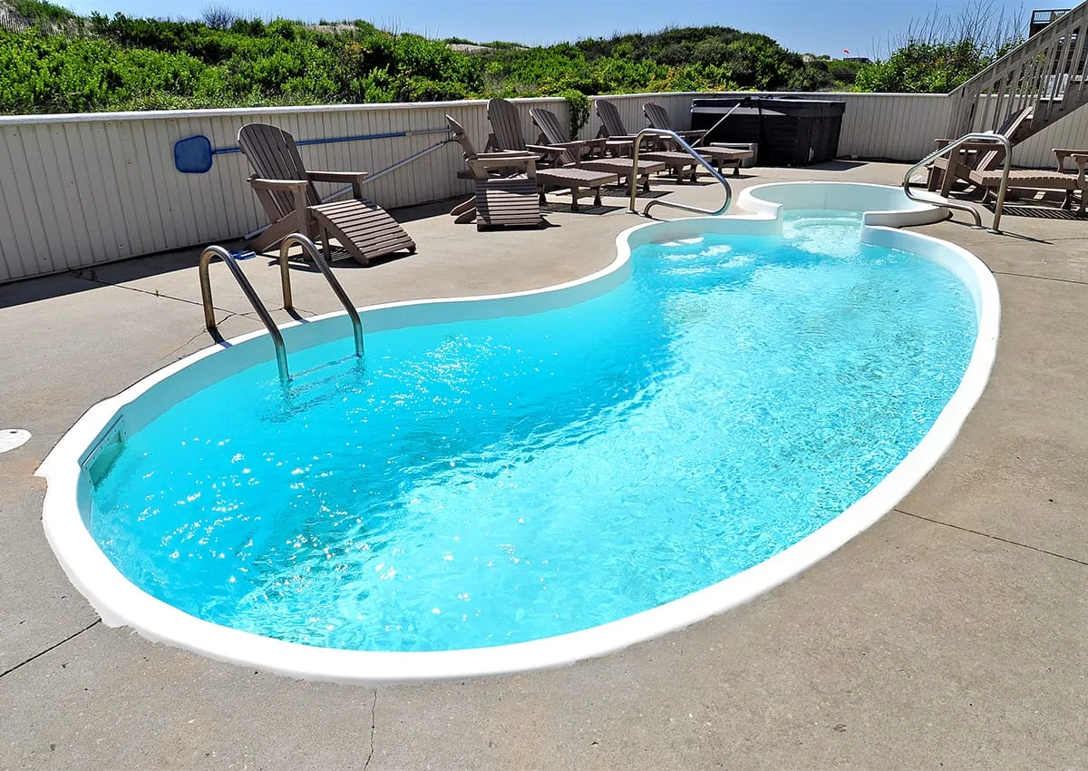 Una piscina al aire libre está rodeada por una terraza pavimentada y asientos.