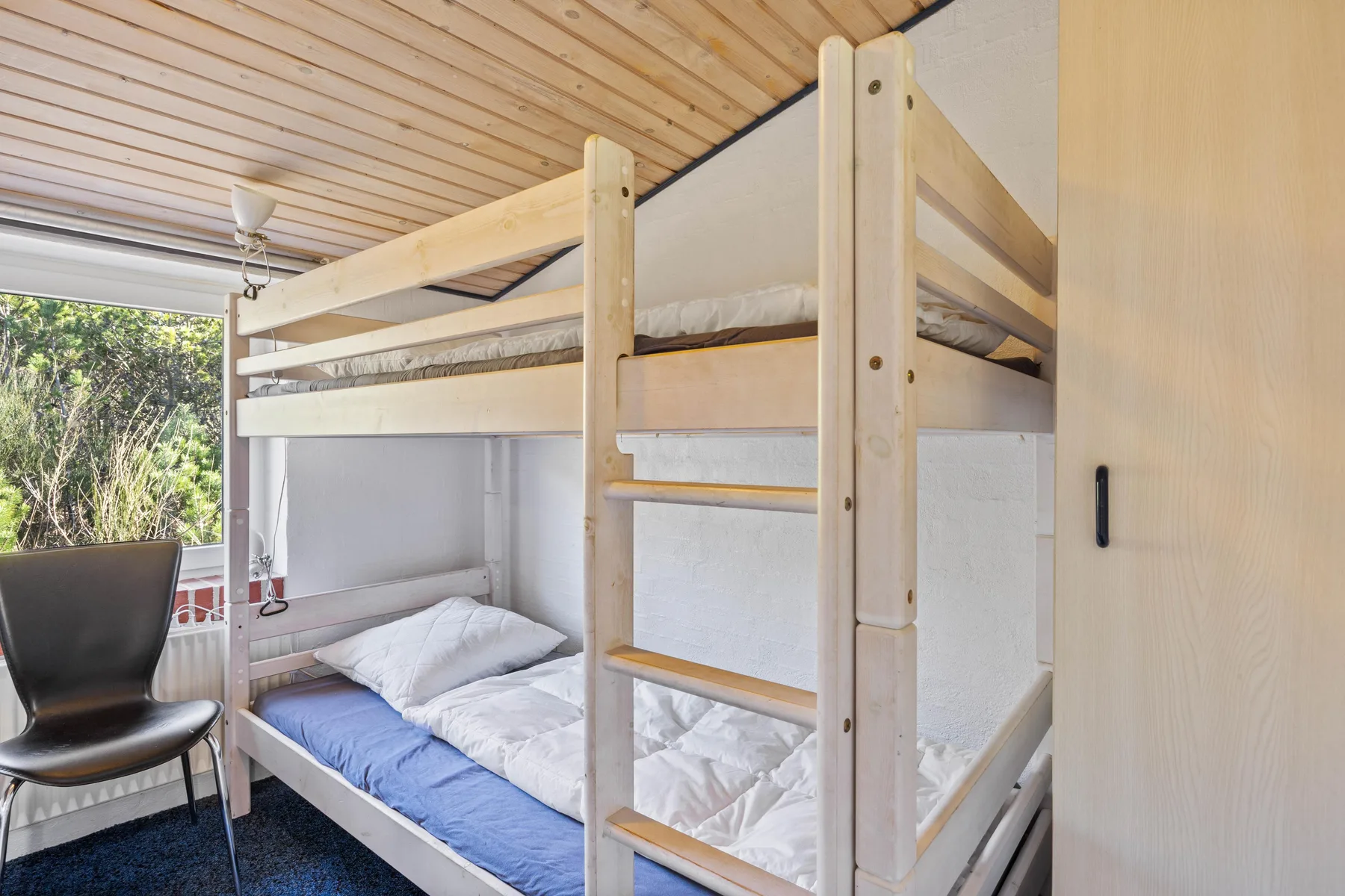 Una litera con ropa de cama blanca está junto a una ventana en un dormitorio.