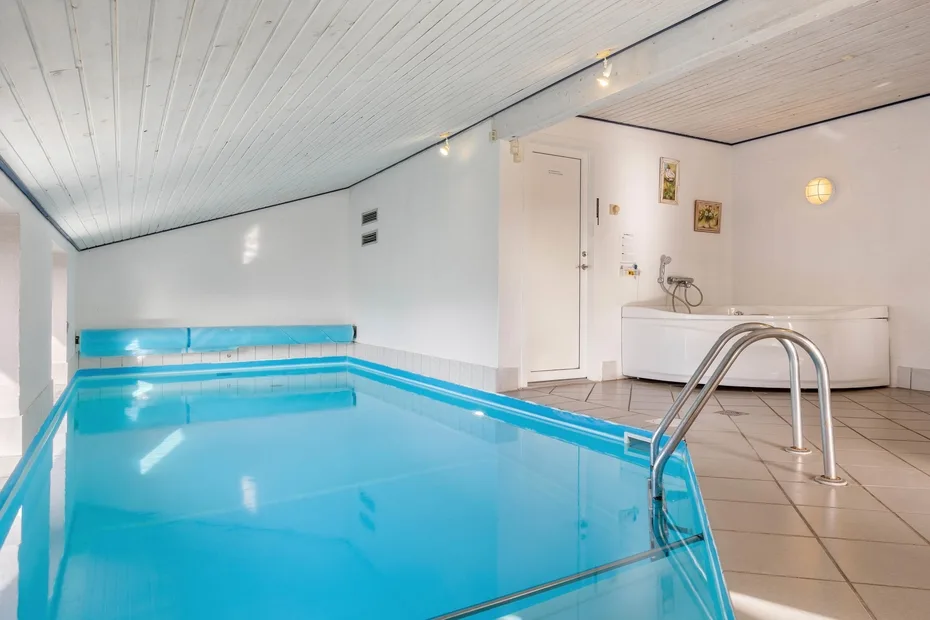 Una piscina cubierta con una escalera metálica y suelo de baldosas.
