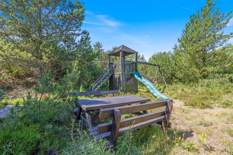 Un parque infantil al aire libre con una estructura de madera y un tobogán entre árboles.