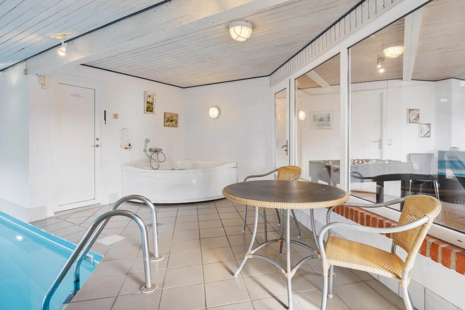 Una zona de piscina interior con una mesa redonda y asientos de mimbre junto al agua.