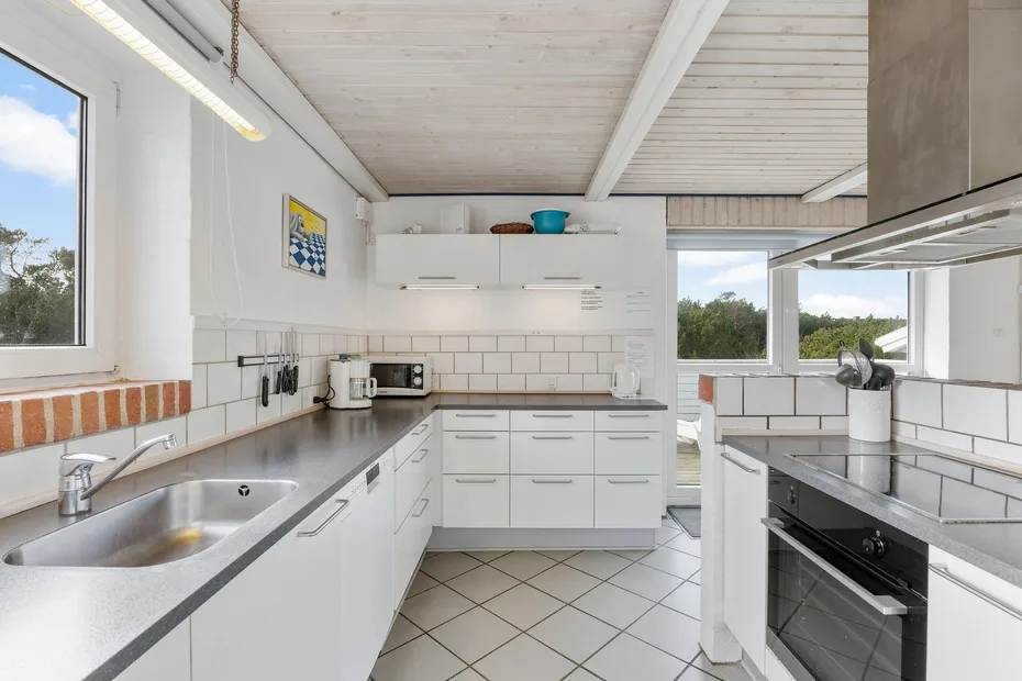 Una cocina luminosa con gabinetes blancos, paredes de azulejos y una encimera larga.