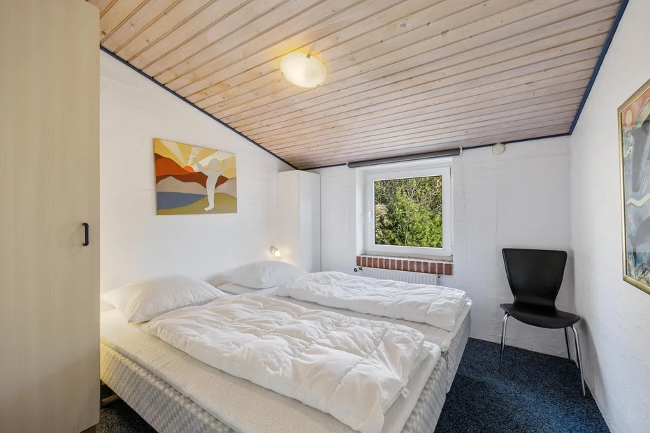 Un dormitorio con camas bajo un techo de paneles de madera y una ventana.
