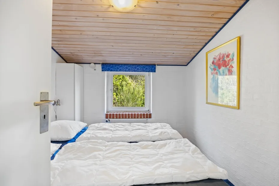 Un dormitorio con ropa de cama blanca, una ventana y un cuadro floral enmarcado.