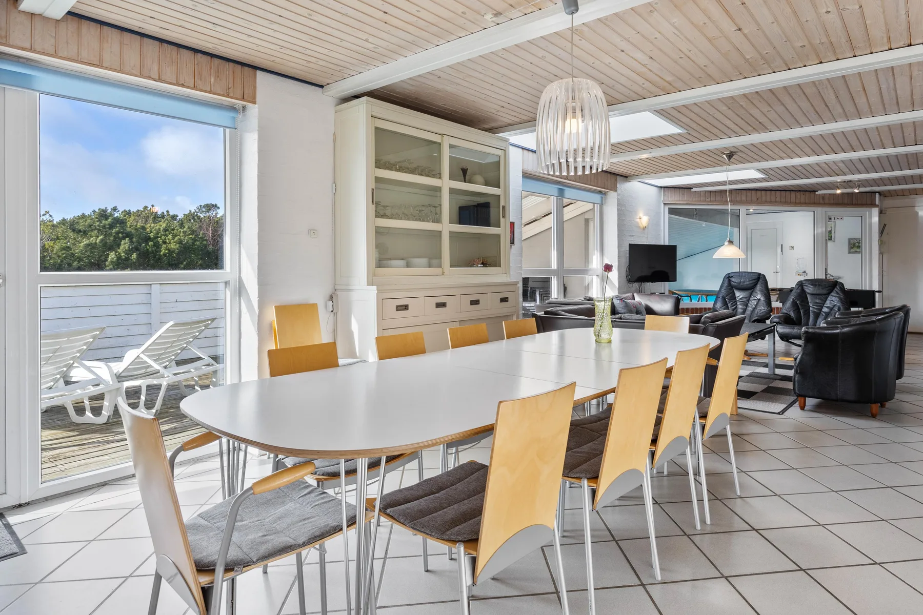 Una luminosa zona de comedor y estar con una mesa larga y asientos junto a grandes ventanales.