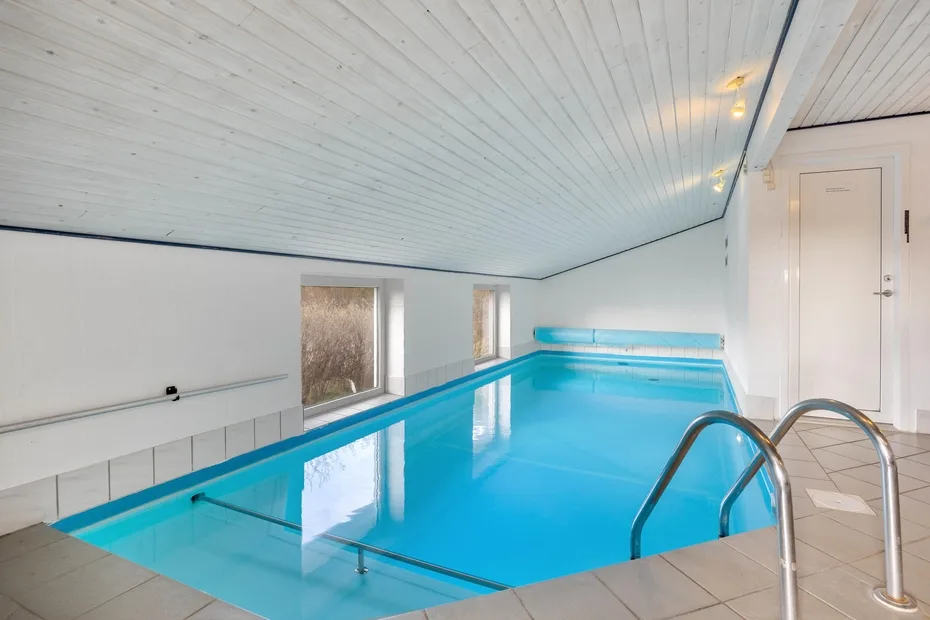 Una piscina cubierta con pasamanos metálicos y ventanas a un lado.