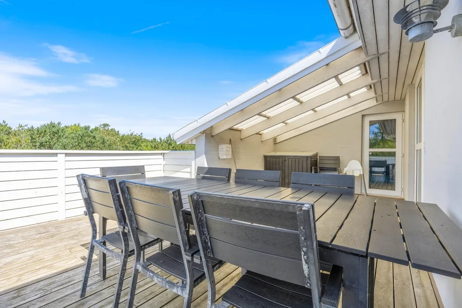 Una terraza exterior con una mesa larga y sillas bajo un techo cubierto.
