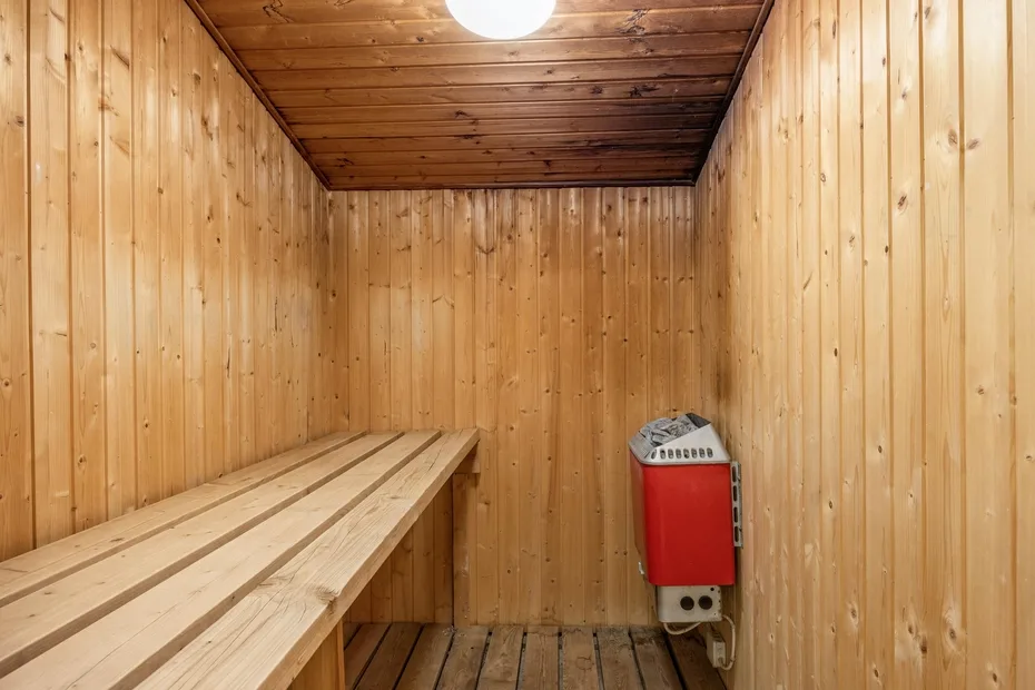 Una sauna revestida de madera tiene asientos escalonados y una estufa.