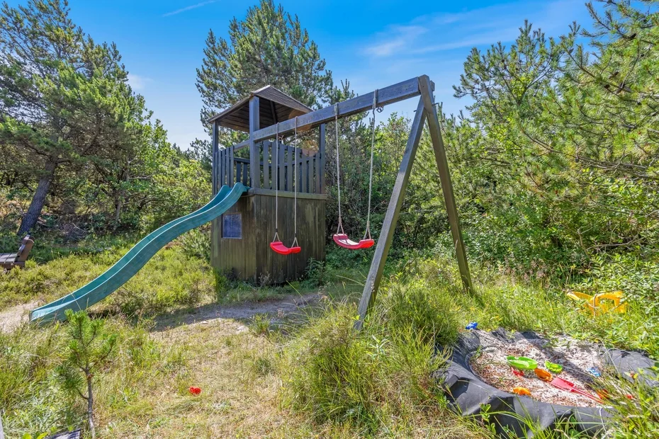Una estructura de juego de madera con tobogán y columpios está entre los árboles.