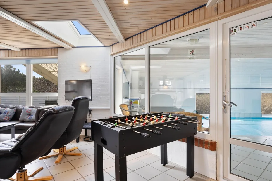 Una sala de estar con futbolín junto a una piscina cubierta.