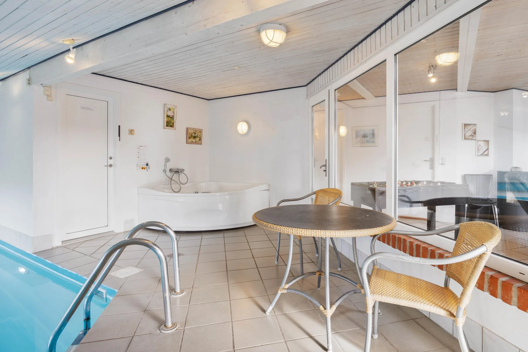 Una zona de piscina cubierta con hidromasaje, suelo de baldosas y asientos.