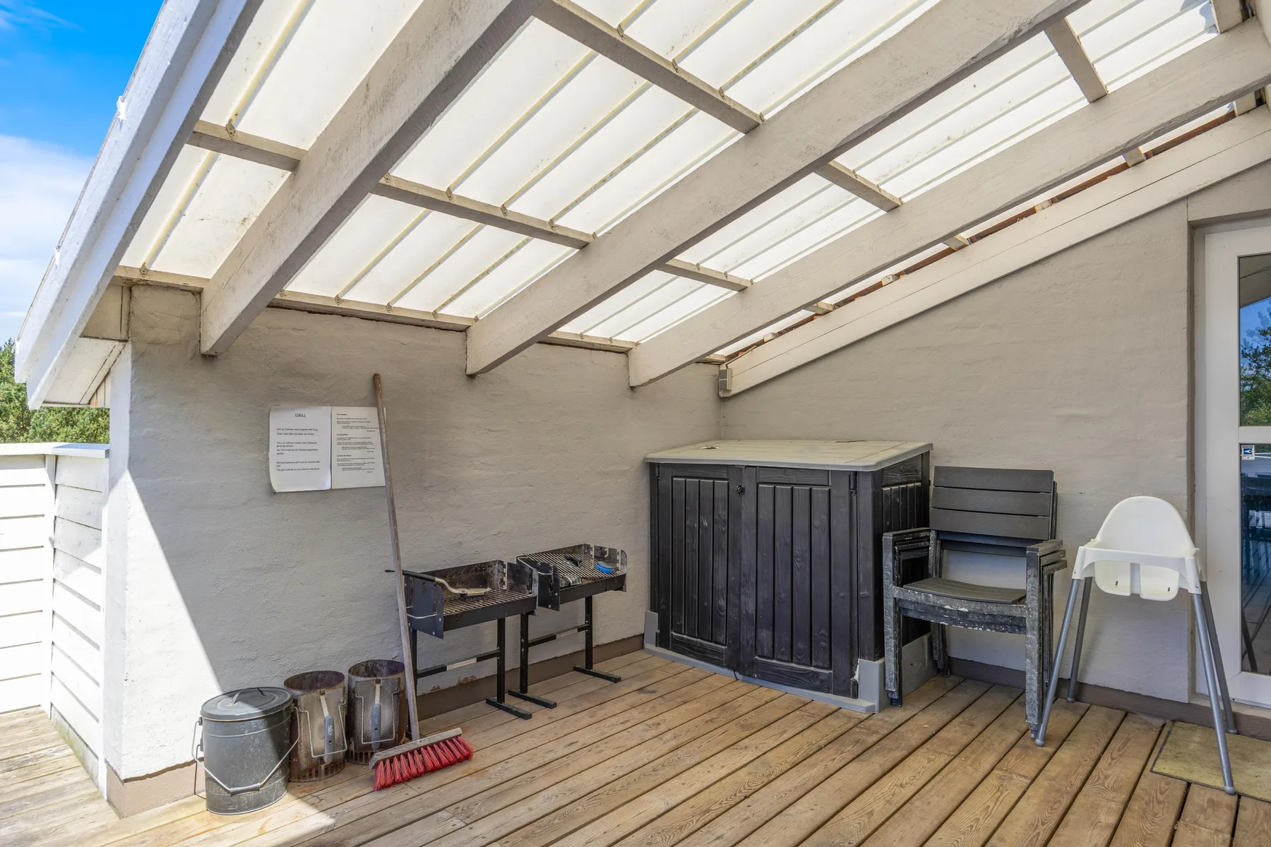 Un patio exterior cubierto con una terraza de madera y armarios de almacenamiento.
