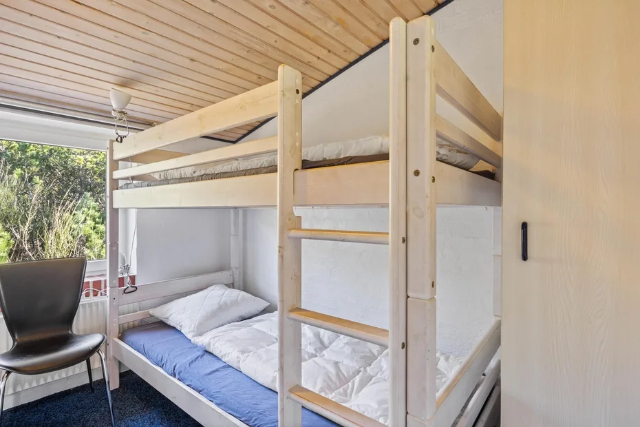 Una litera con ropa de cama blanca está bajo un techo inclinado de madera.