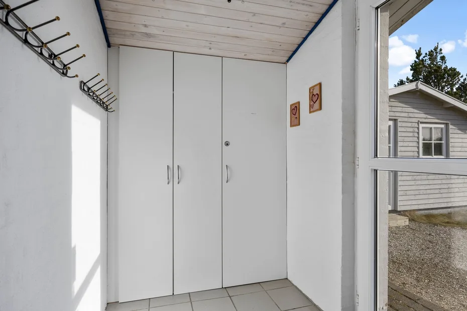 Una entrada luminosa con armarios blancos empotrados y ganchos en la pared.