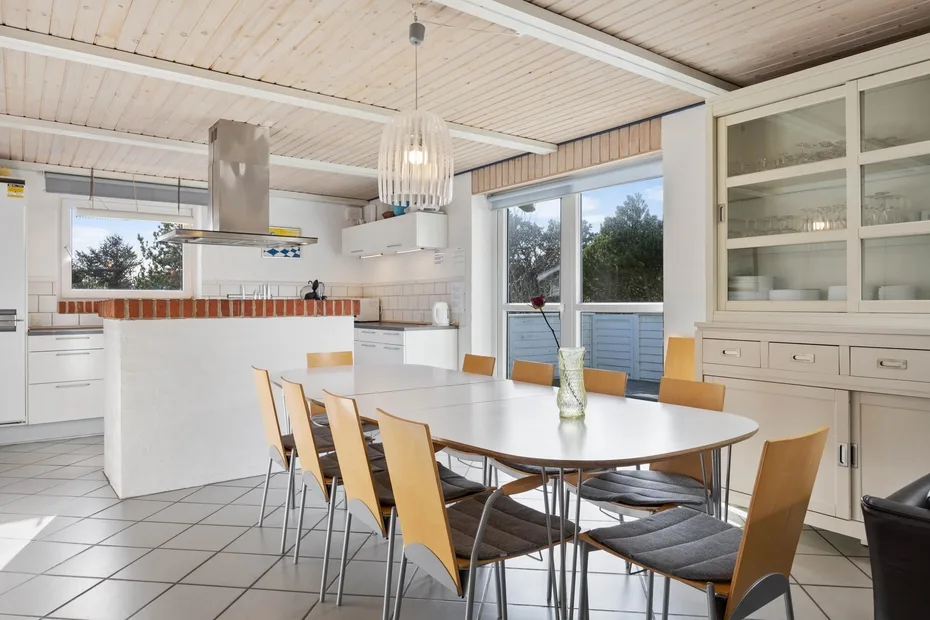 Un comedor luminoso con una mesa larga, sillas y ventanales.