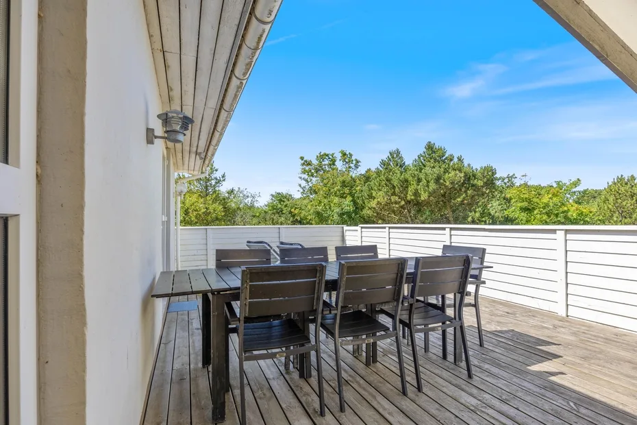 Zona de comedor al aire libre con mesa y asientos en una terraza de madera.