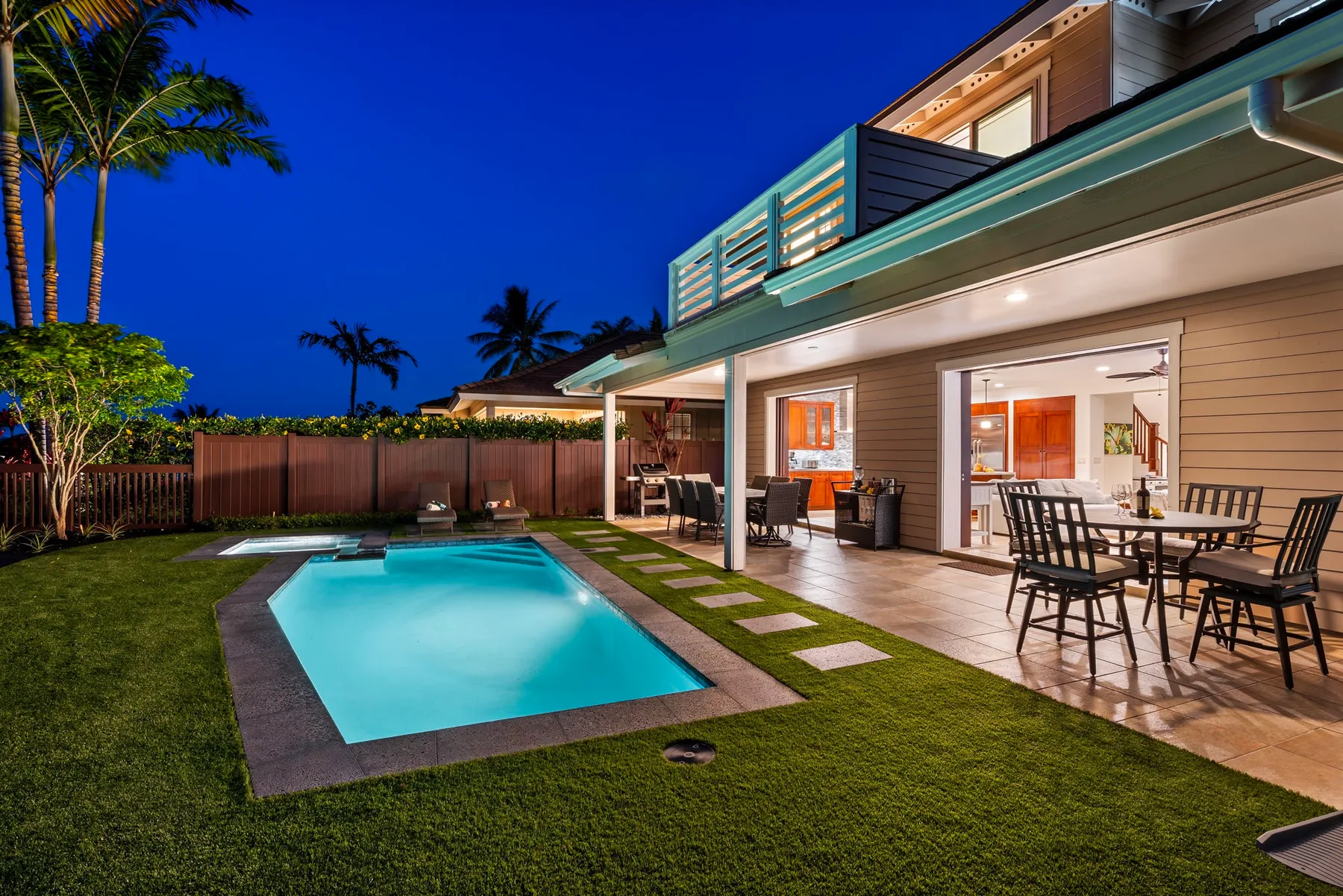 A modern house opens onto a patio beside a swimming pool and lawn.