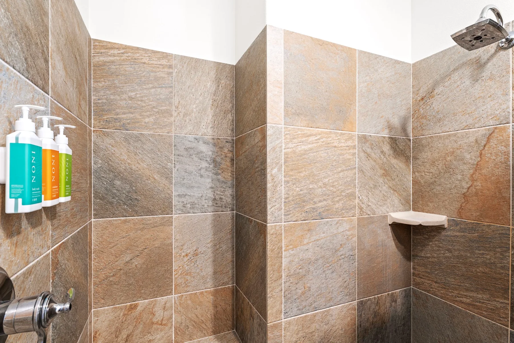 A tiled shower with a wall-mounted showerhead and soap dispensers.