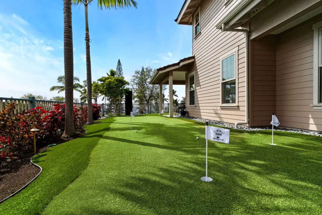 A landscaped lawn beside a house, with palms and garden beds along the edge.
