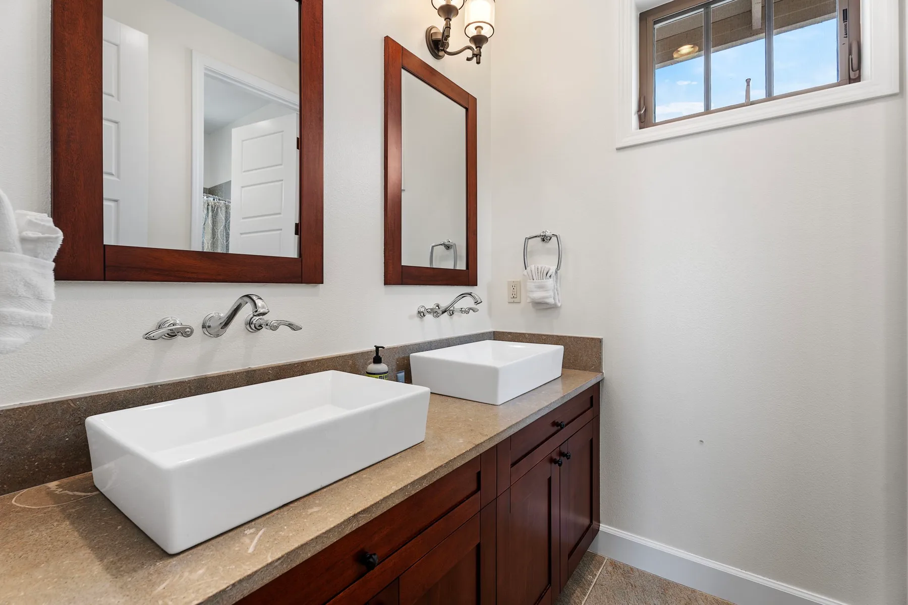 A bright bathroom with two sinks, wood cabinetry, and a window.