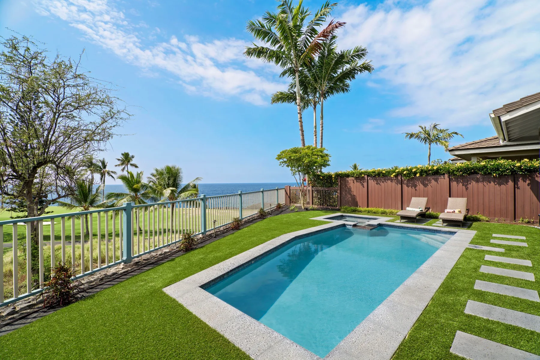 A rectangular swimming pool sits in a grassy yard beside a coastal view.
