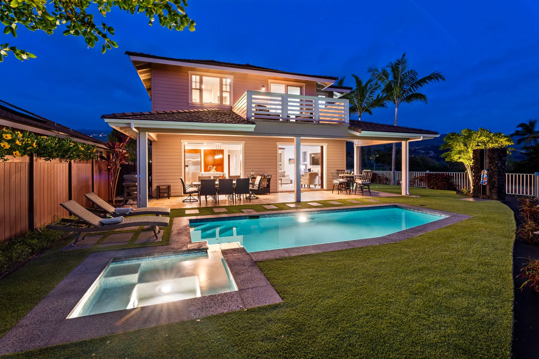A two-story house overlooks a lit swimming pool and patio at dusk.
