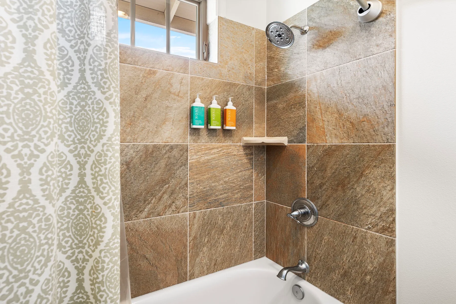 A tiled bathroom shower area with a showerhead above the bathtub.