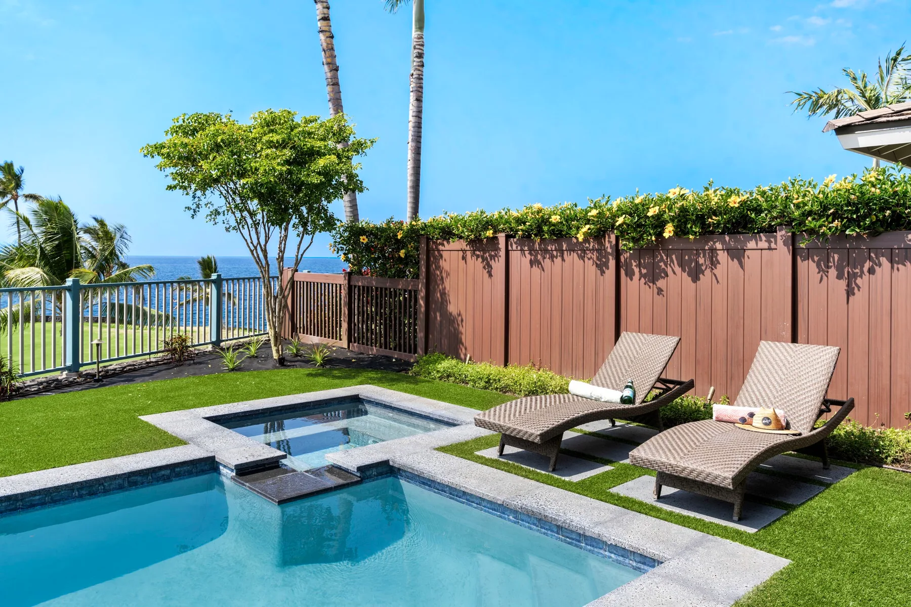 An outdoor swimming pool with lounge seating beside a garden fence.