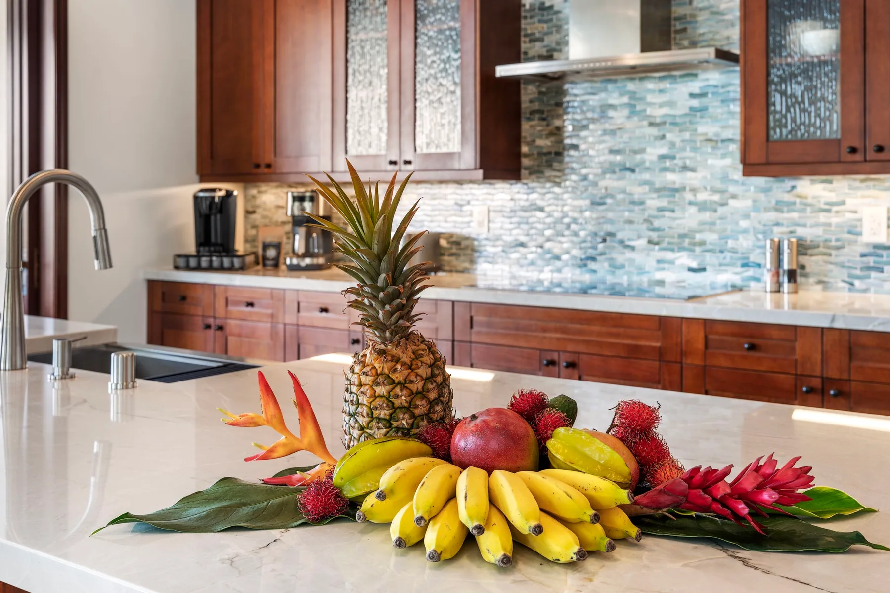 A kitchen counter displays a pineapple, bananas, and other fruit.