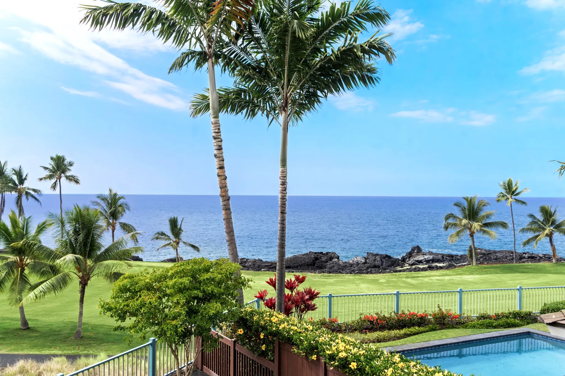 A landscaped tropical shoreline overlooks the ocean, with a pool in the foreground.