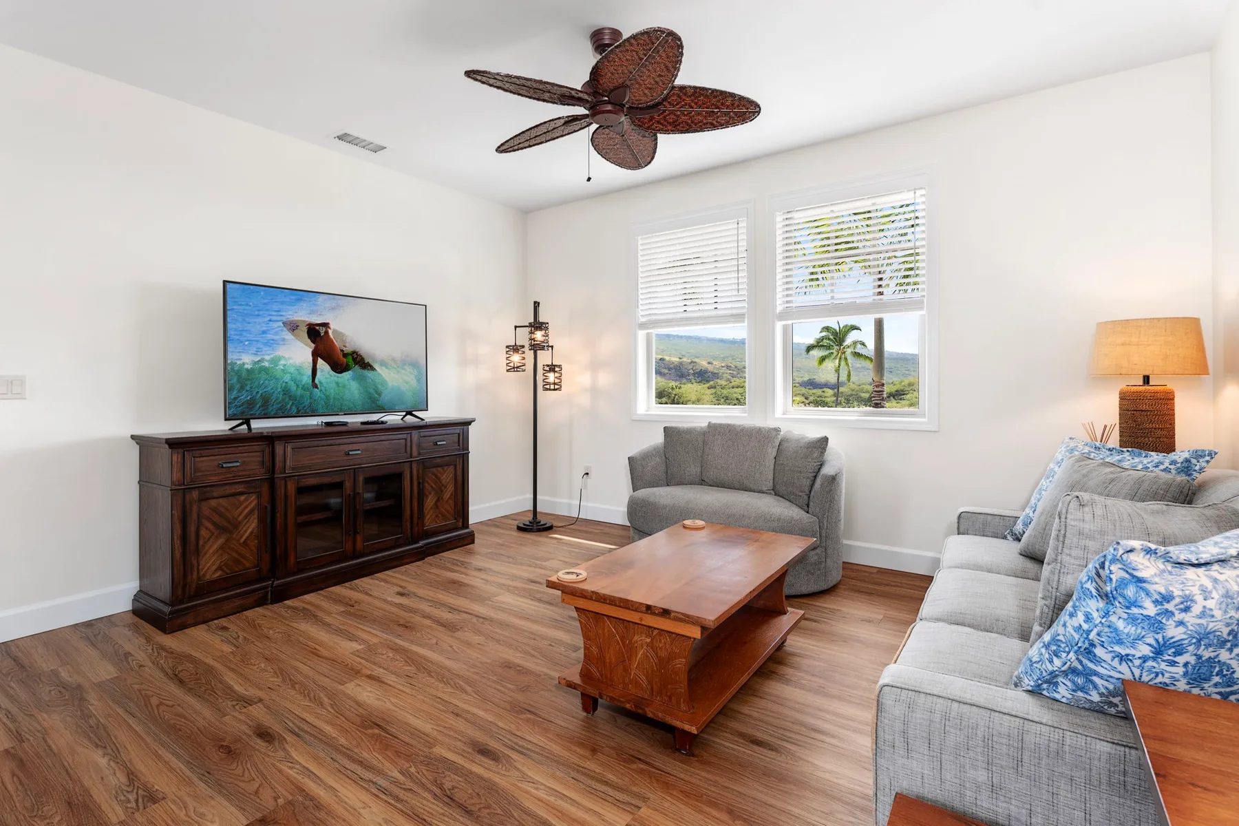 A bright living room with seating, a wooden coffee table, and windows.