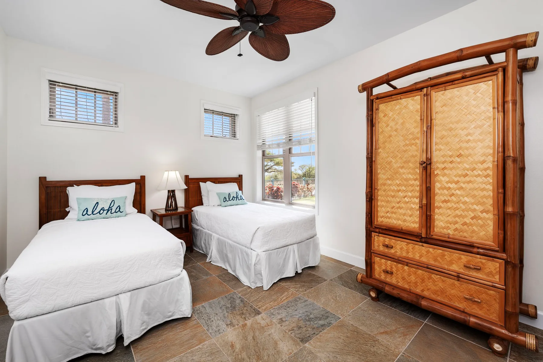 A bright bedroom with two beds, a ceiling fan, and a woven wooden wardrobe.
