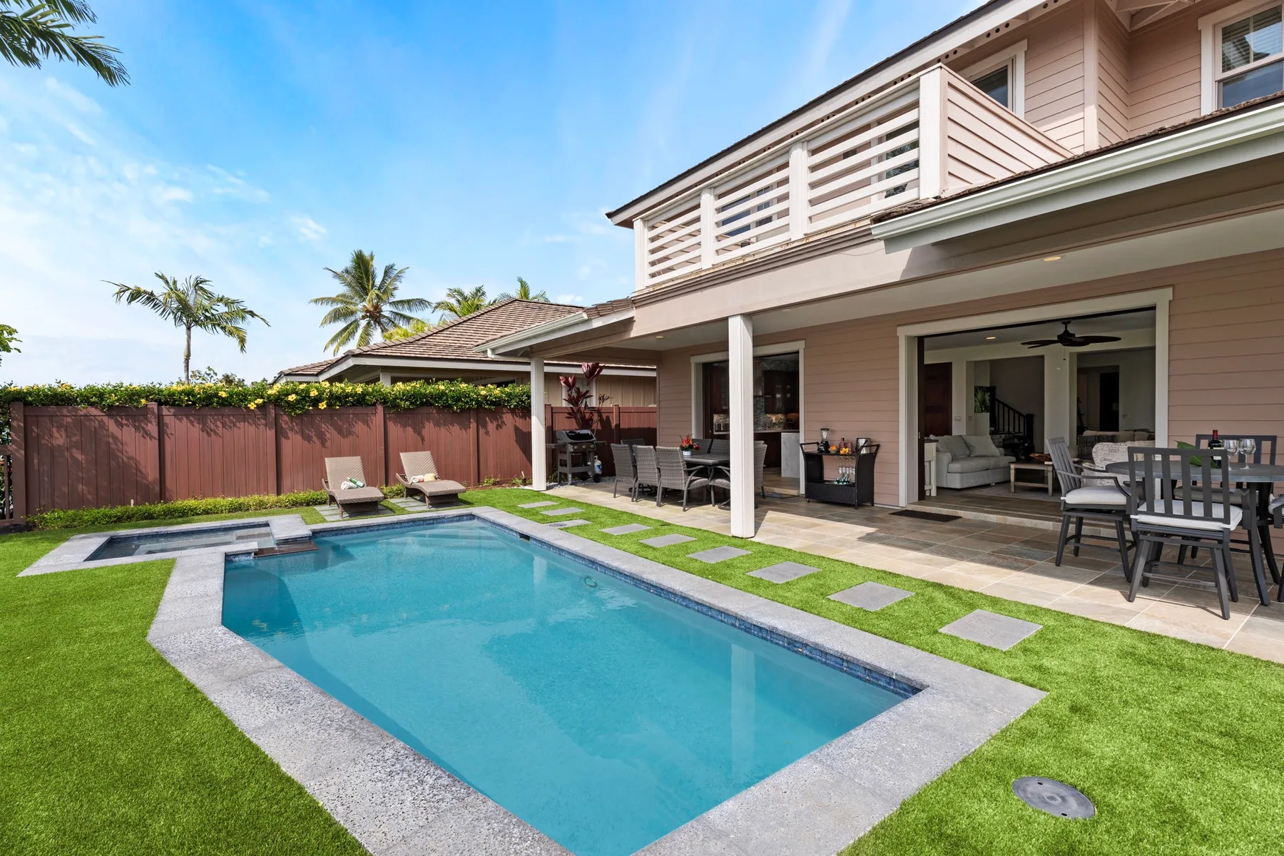 A backyard swimming pool sits beside a covered patio with outdoor seating.