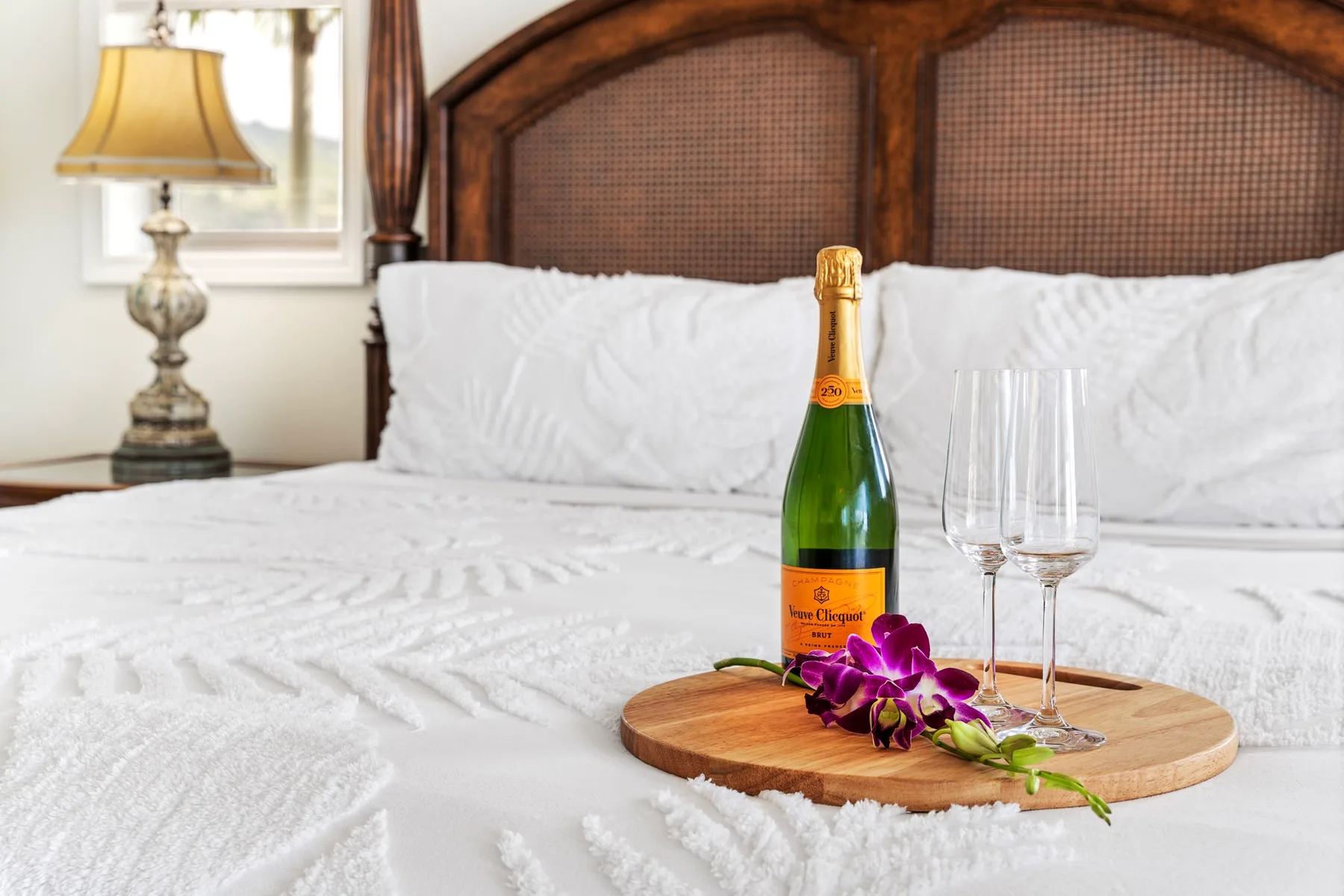 A neatly made bed with a bottle of sparkling wine and glasses on a tray.