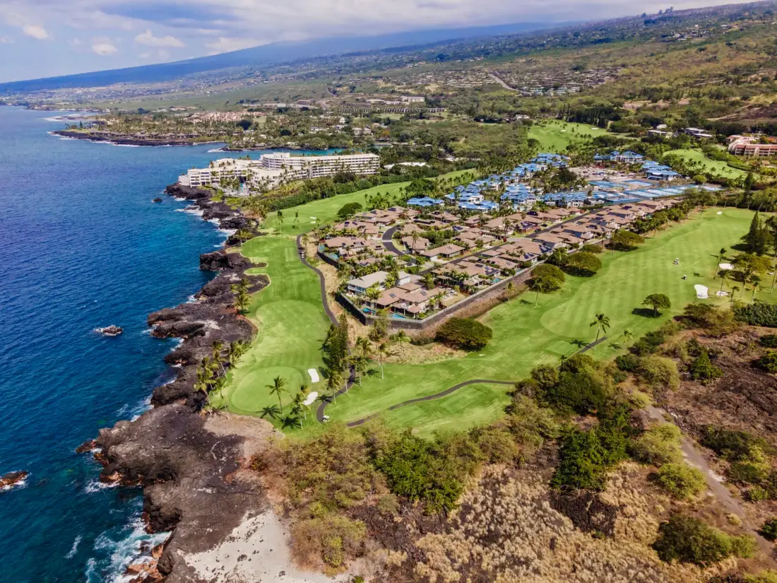 Aerial view of a coastal resort area with green lawns beside the ocean.