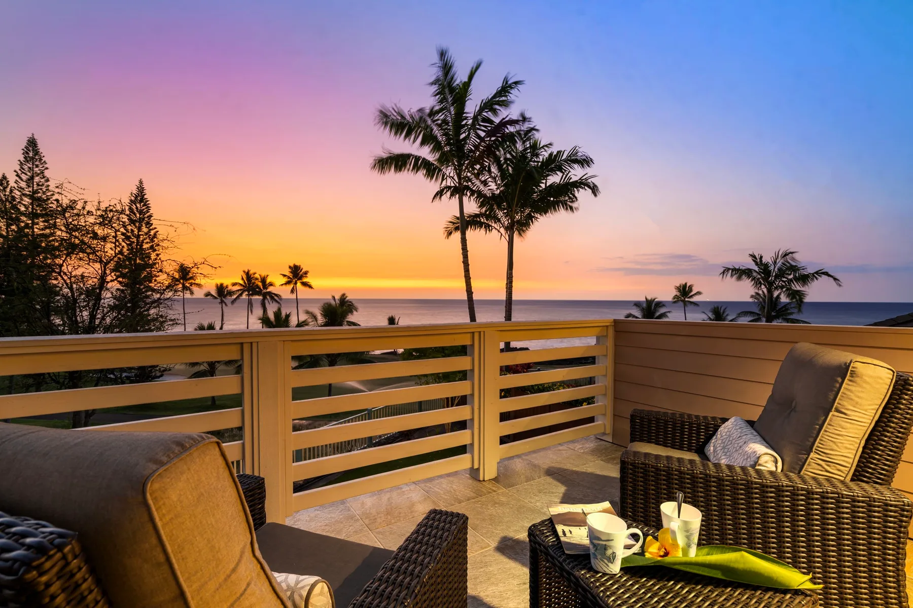 A patio seating area overlooks the ocean beneath a colorful sunset sky.