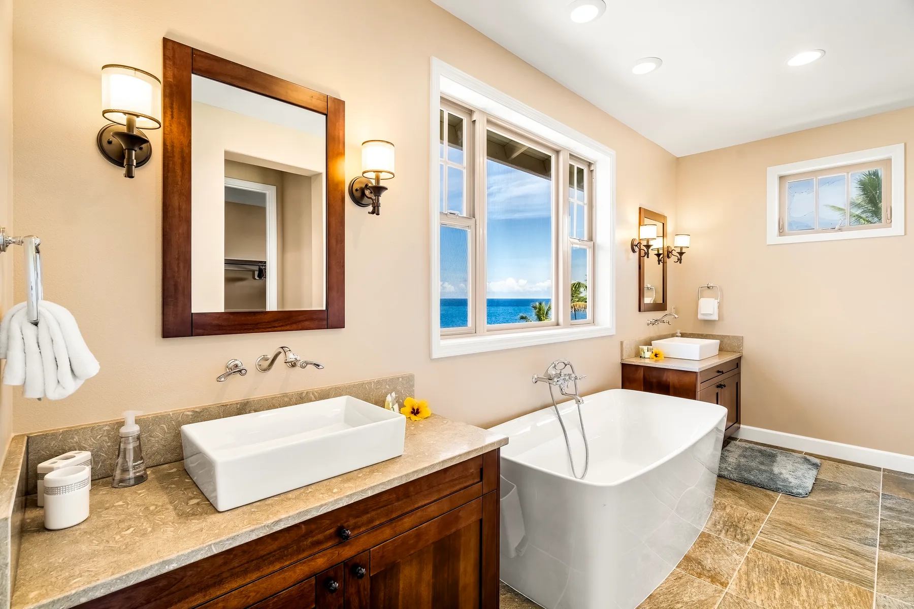 A bright bathroom with a freestanding tub, vanity, and windows overlooking the sea.