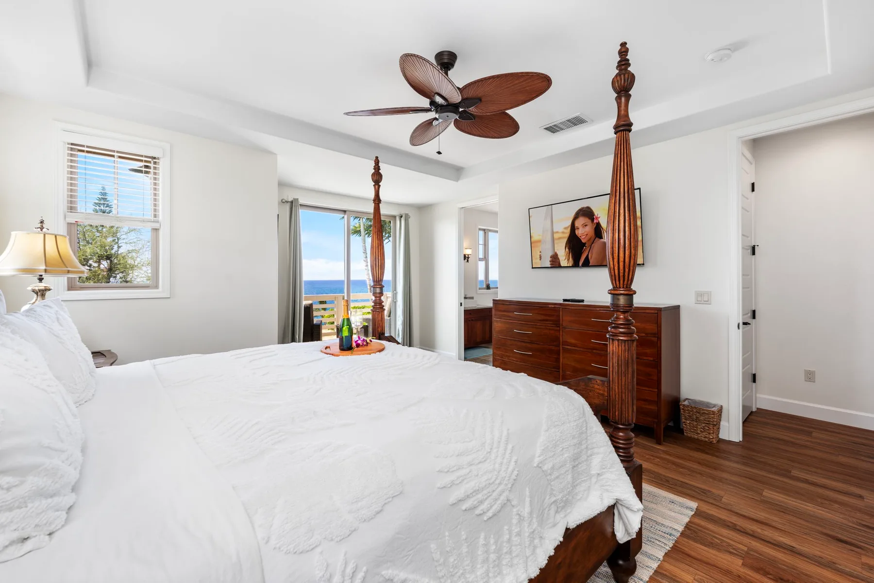 A bright bedroom with a white bed, a wooden dresser, and a ceiling fan.
