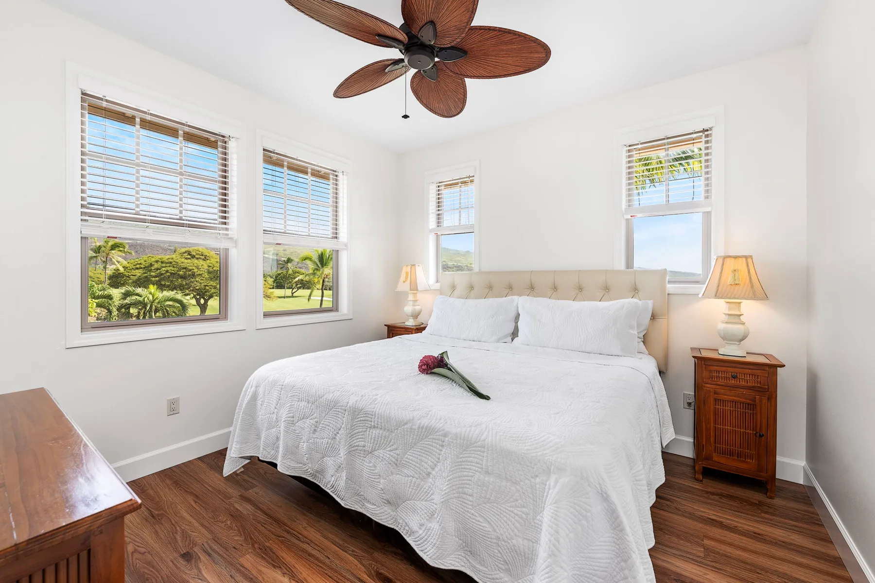 A bright bedroom with a neatly made bed beneath a ceiling fan.