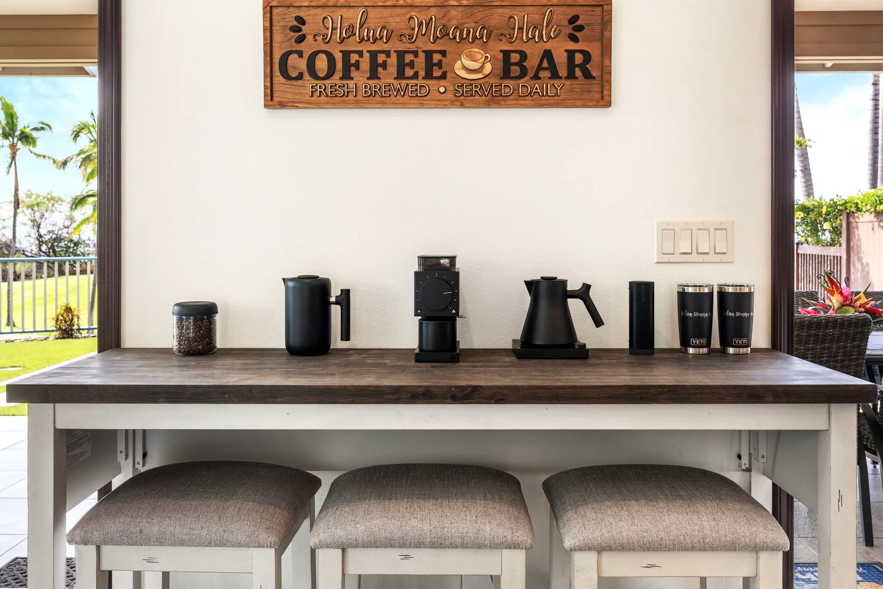 A coffee bar with brewing equipment sits on a counter above three stools.