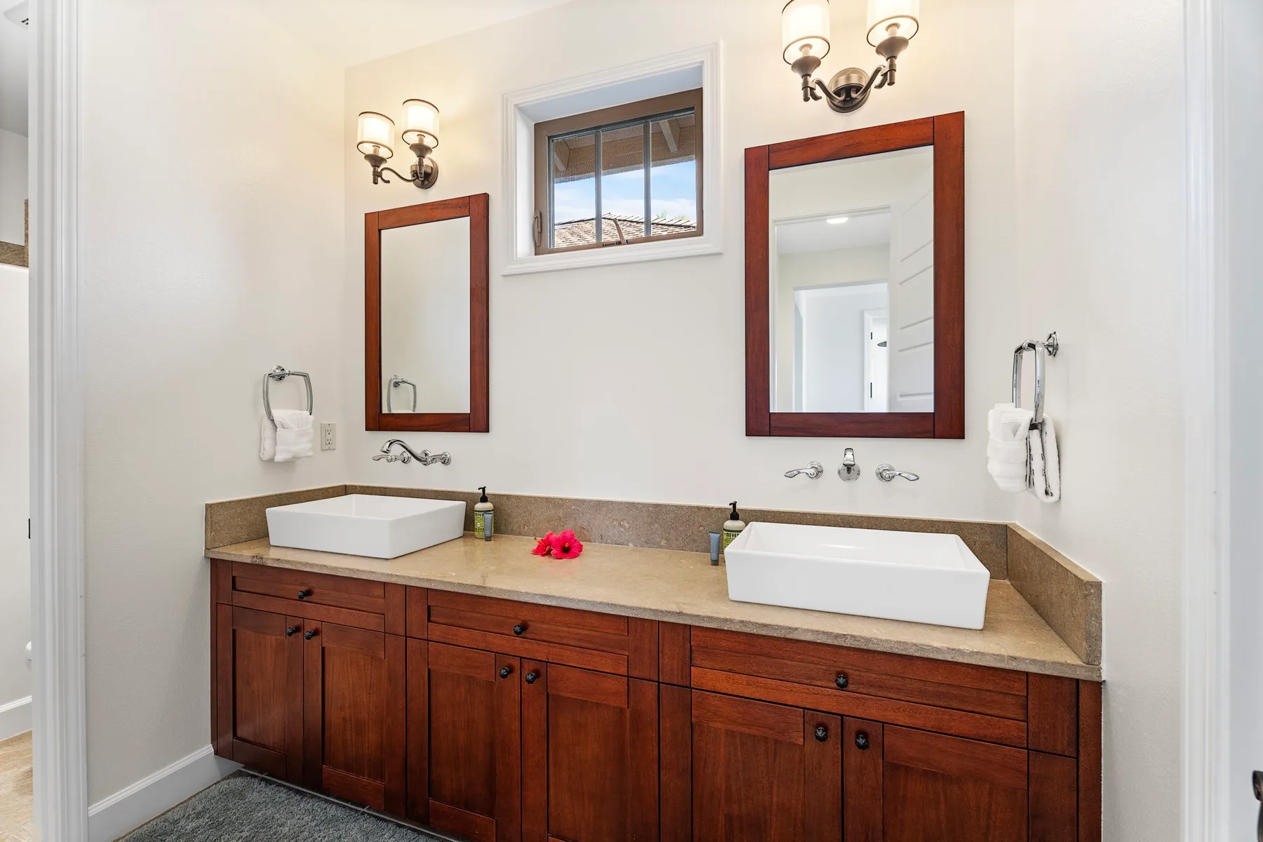 A bathroom vanity with two sinks, mirrors, and a window above.