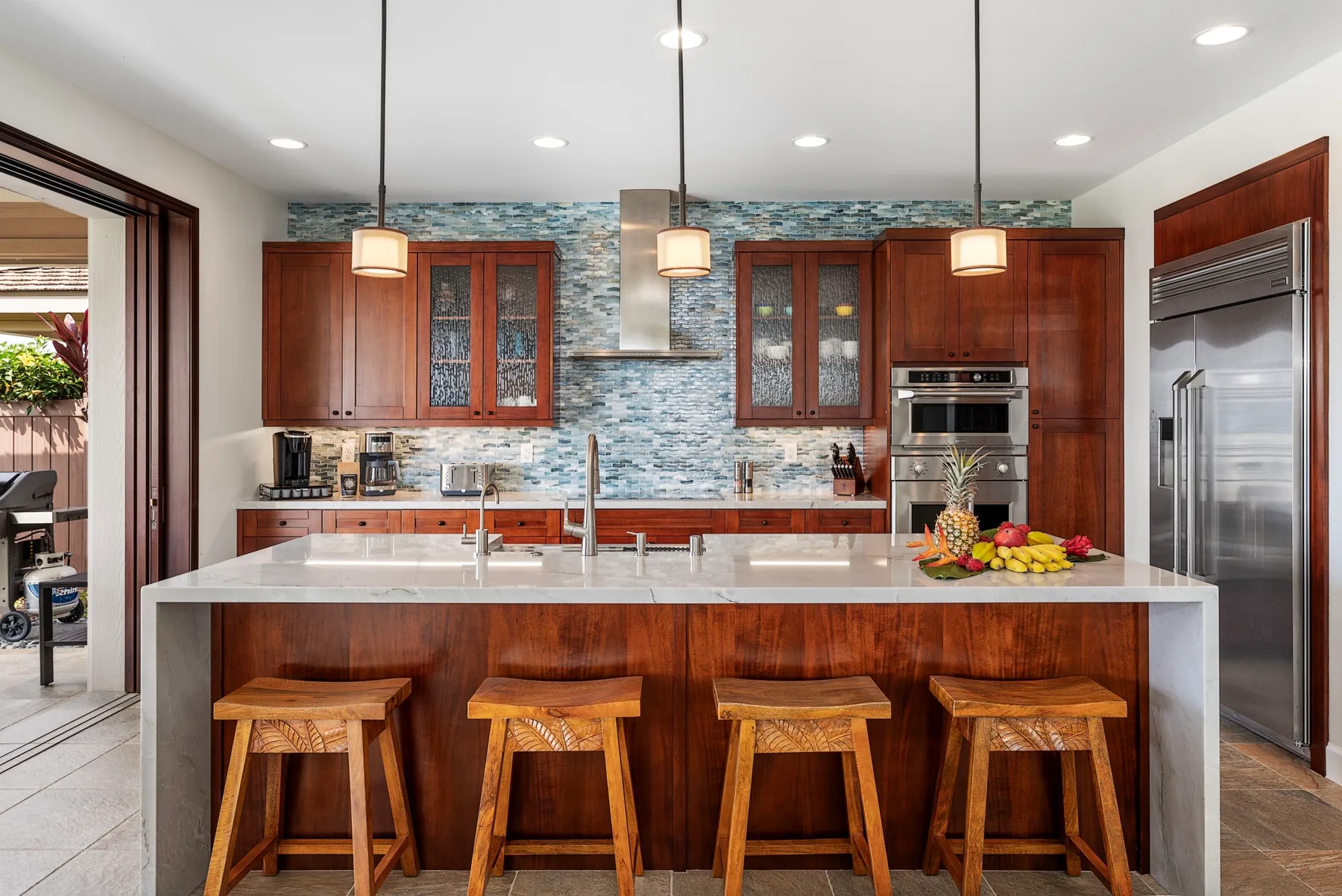 A modern kitchen with a large island, wooden seating, and stainless steel appliances.