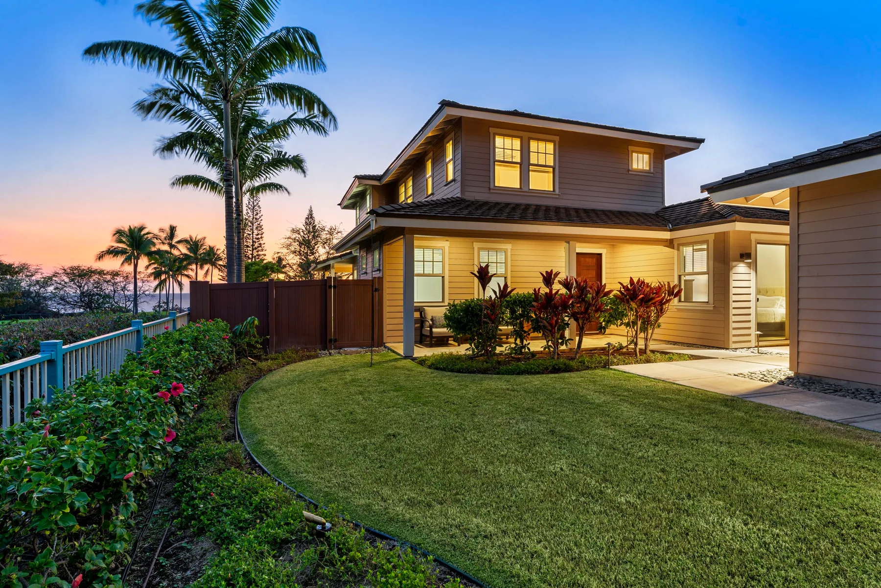 A two-story house with a lawn and tropical plants at dusk.