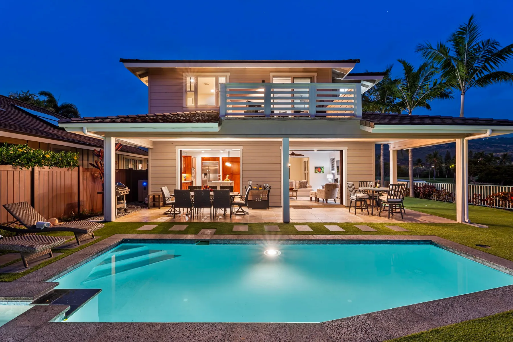 A modern house opens onto an illuminated swimming pool and outdoor dining area at dusk.