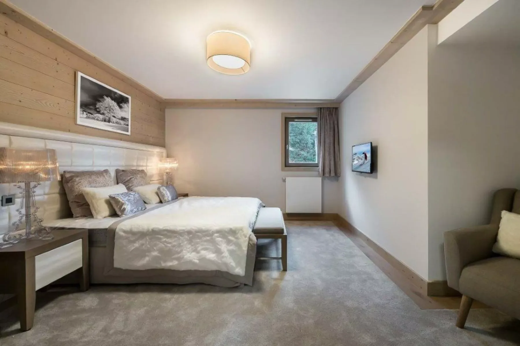 A bedroom with a made bed and a window overlooking greenery.