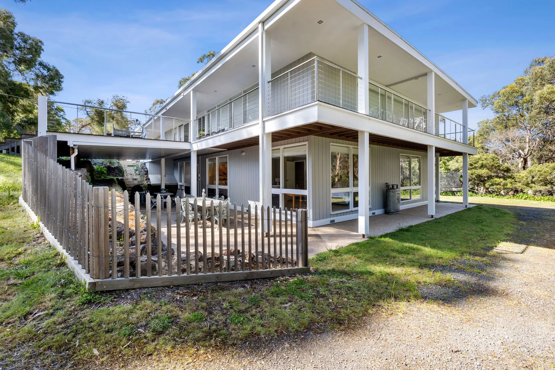 A two-story house with covered balconies stands beside a fenced patio.
